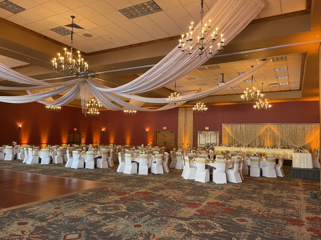 Many tables with white chairs on ornate carpet design and golden uplighting on walls